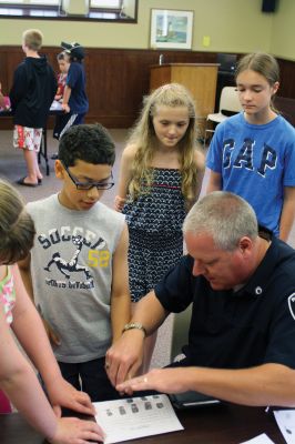 CSI Chemistry
During the CSI Chemistry event at the Mattapoisett Free Library on August 1, Rochester Police Chief Paul Magee fingerprinted the kids during a fingerprinting demonstration, and Brendan Taylor, age 10, was the first one up. Chief Magee’s son Rob Magee led the presentation, which was one of the library’s exciting children’s summer events. Photo by Jean Perry
