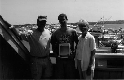 041504-3
Craig Mechler of New England Home poses here with his son Ben, mother-in-law Ellie Haines, and a copy of The Wanderer at the Montauk Yacht Club during the first annual I Love N.Y. Hook and Release International Brits vs. Yanks Shark Fishing Tournament. (Photo courtesy of Craig Mechler). 4/15/04 edition
