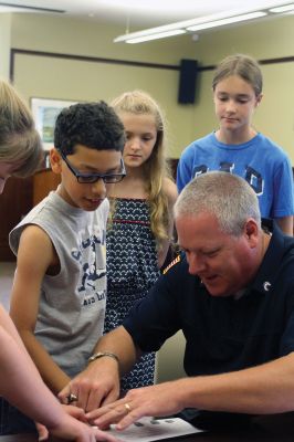 CSI Chemistry
During the CSI Chemistry event at the Mattapoisett Free Library on August 1, Rochester Police Chief Paul Magee fingerprinted the kids during a fingerprinting demonstration, and Brendan Taylor, age 10, was the first one up. Chief Magee’s son Rob Magee led the presentation, which was one of the library’s exciting children’s summer events. Photo by Jean Perry
