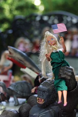 Plasticastrophe! 
It doesn’t matter that she’s about to be eaten by King Kong – Barbie stays smiling, as do all the Barbies planted in Teresa Dall’s “Barbie Garden” of 16 North Street in Mattapoisett. Here, Barbie manages to display a little Fourth of July spirit while making imminent annihilation appear blissful. Photo (and flag accessory) by Jean Perry - July 5, 2018 edition
