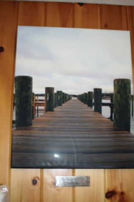 Mattapoisett Harbormaster
Mattapoisett Harbormaster Jill Simmons has become a de facto art museum curator since the town acquired prints and photographs that now grace the walls of the tiny harbormaster’s office at Shipyard Park. Local photographer Misty King has several of her pieces on display, along with two pieces by USCG’s artist Michael Mazur. Mazur’s pieces depict scenes from the 2003 Bouchard oil spill off West Island. Simmons welcomes the public to stop by and take a look at the mini art installation. Photo by Marilou Newel
