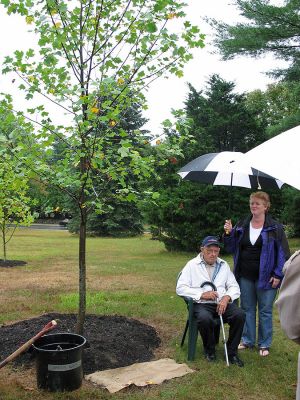 Church Tree Dedication
Following a longstanding tradition, the Trustees and Friends of the Joseph H. Plumb Memorial Library dedicated a tulip tree in memory of Katherine Church. Ms. Church had been a Trustee for many years, as well as being a faithful and longtime member of the Friends of the Library. Mr. George Church (seated) and family members and friends, as well as Trustees and members of the Friends, listened while Trustee Lena Bourque (standing behind Mr. Church) spoke of Ms. Churchs dedication. (Photo by Wendy Keeler).
