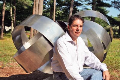 A Tribute to Heroes
Mattapoisett artist and sculptor Keith Francis poses with the sculpture he designed and built in tribute to the Worcester Six, the firefighters who perished in the tragic Worcester Warehouse fire on December 3, 1999. The massive one-ton sculpture now sits in his North Street backyard in clear view of several neighbors who are either firefighters, retired firefighters or relatives of firefighters. (Photo by Robert Chiarito).
