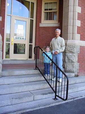 Library Leaning
The Mattapoisett Free Public Library Trustees recently announced the installation of a new handrail which should afford easier access to the library in its temporary quarters at Center School, especially for those citizens who have had difficulty climbing the outside staircase. The first patrons to officially use this new handrail were longtime library volunteer Papa John Hilsabeck and his 3-year old granddaughter Rachel Foye, pictured here.
