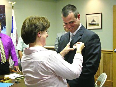 New Deputy in Town
Susan Murray pins a badge on her son, newly-appointed Mattapoisett Deputy Fire Chief Andrew Murray, during the recent Board of Selectmens meeting where Mr. Murray was formally appointed to the position. Fire Chief Ron Scott and members of the Mattapoisett Police and Fire Departments were also on hand as Mr. Murray worked for both departments. (Photo by Kenneth J. Souza).
