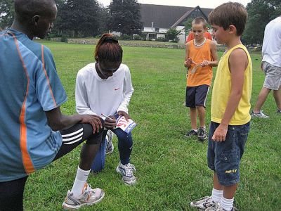 Kenyan Couple
Kenyan runner Nicholas Kamakya (far left) and his wife Angelina Mutuku sign autographs for the kids during the final Marion Mile Just for Kids competition held last week at Tabor Academy. The couple talked about running in Kenya and led the kids through warm-ups and stretching prior to jogging along in the back of the pack with some of the youngest competitors. (Photo courtesy of Chris Adams).
