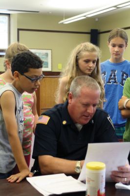 CSI Chemistry
During the CSI Chemistry event at the Mattapoisett Free Library on August 1, Rochester Police Chief Paul Magee fingerprinted the kids during a fingerprinting demonstration, and Brendan Taylor, age 10, was the first one up. Chief Magee’s son Rob Magee led the presentation, which was one of the library’s exciting children’s summer events. Photo by Jean Perry

